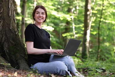 Photo of Smiling freelancer working with laptop in forest. Remote job