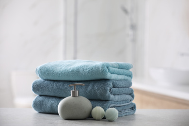 Photo of Stack of fresh towels, soap dispenser and bath bombs on table indoors