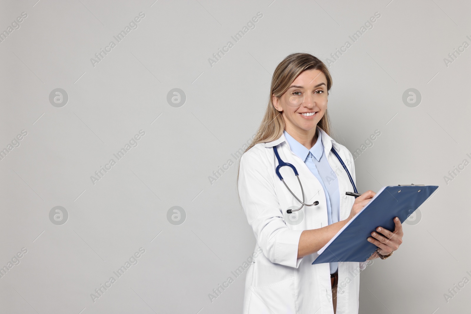 Photo of Portrait of happy doctor with stethoscope and clipboard on light grey background, space for text