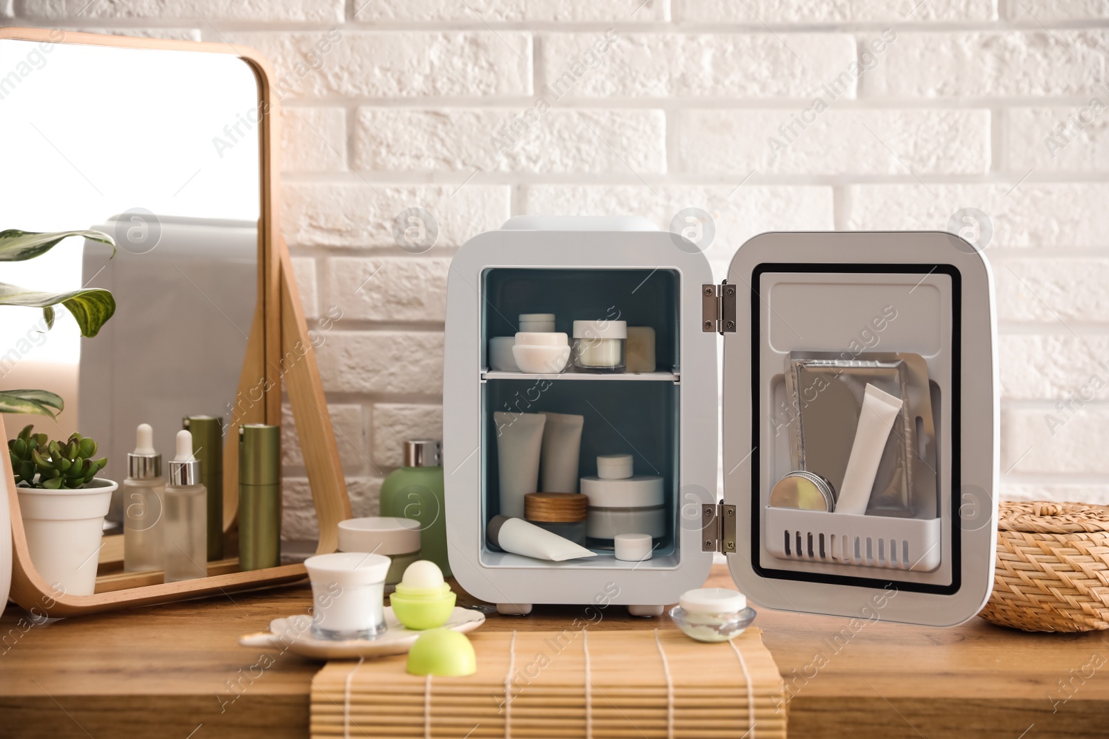 Photo of Mini fridge with cosmetic products on wooden vanity table