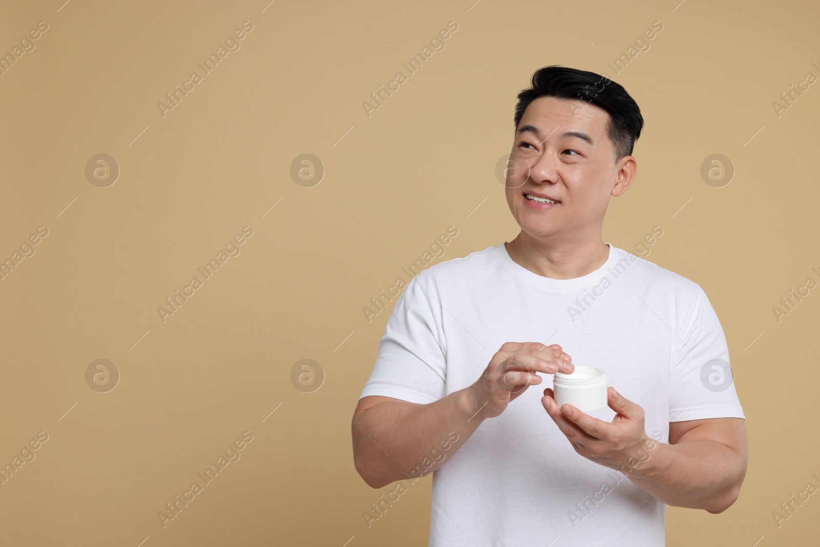 Photo of Handsome man with jar of body cream on light brown background. Space for text