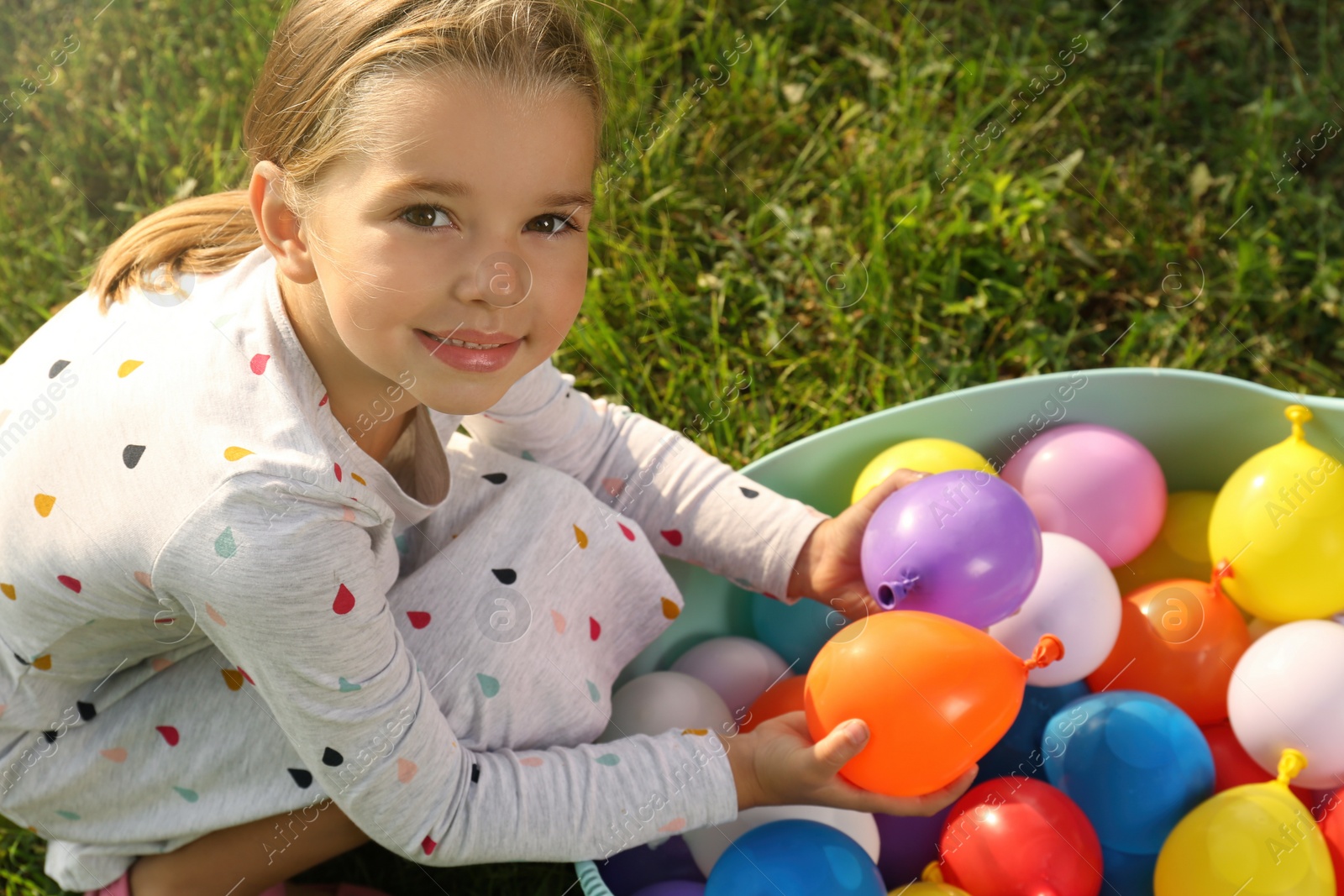 Photo of Little girl with basin of water bombs on green grass, above view