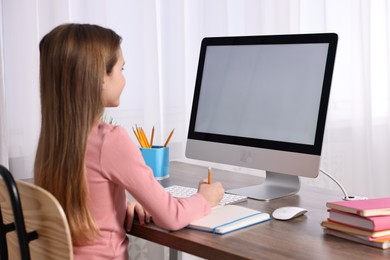 Photo of E-learning. Cute girl taking notes during online lesson at table indoors