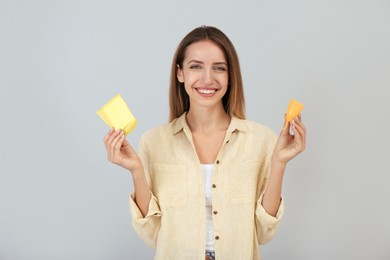Happy young woman with menstrual cup and disposable pad on grey background