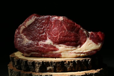 Piece of raw beef meat on decorative wooden stand against black background, closeup