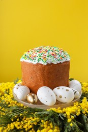 Traditional Easter cake with sprinkles, painted eggs and beautiful spring flowers on yellow background, closeup