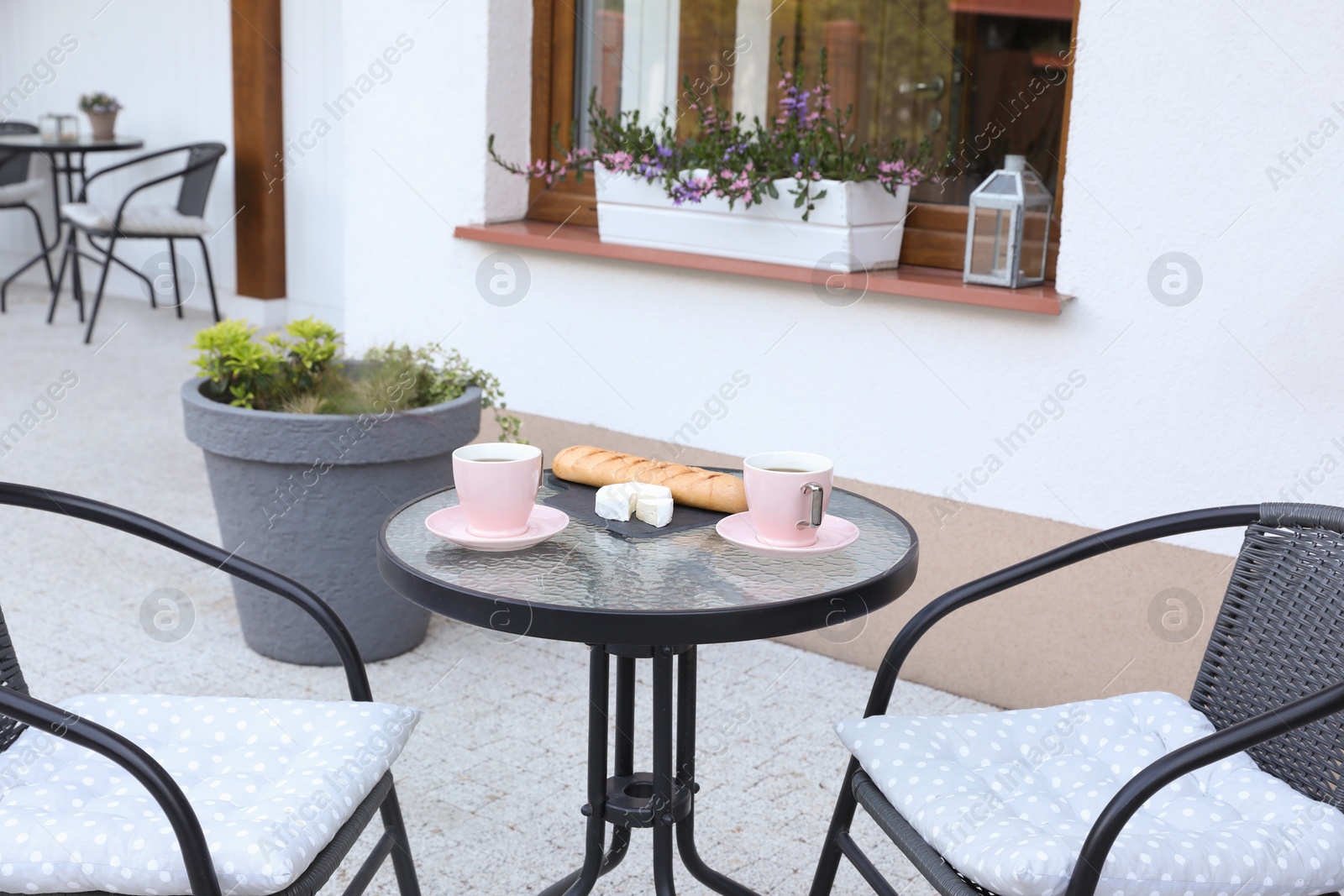 Photo of Cups of coffee, bread and cheese on glass table. Relaxing place at outdoor terrace