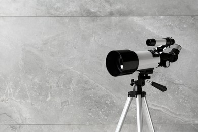 Photo of Tripod with modern telescope near grey wall, closeup. Space for text