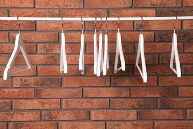 Photo of White clothes hangers on rail near red brick wall. Space for text