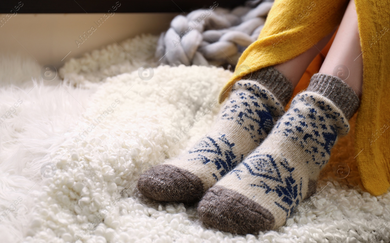 Photo of Woman wearing knitted socks on window sill indoors, closeup. Warm clothes