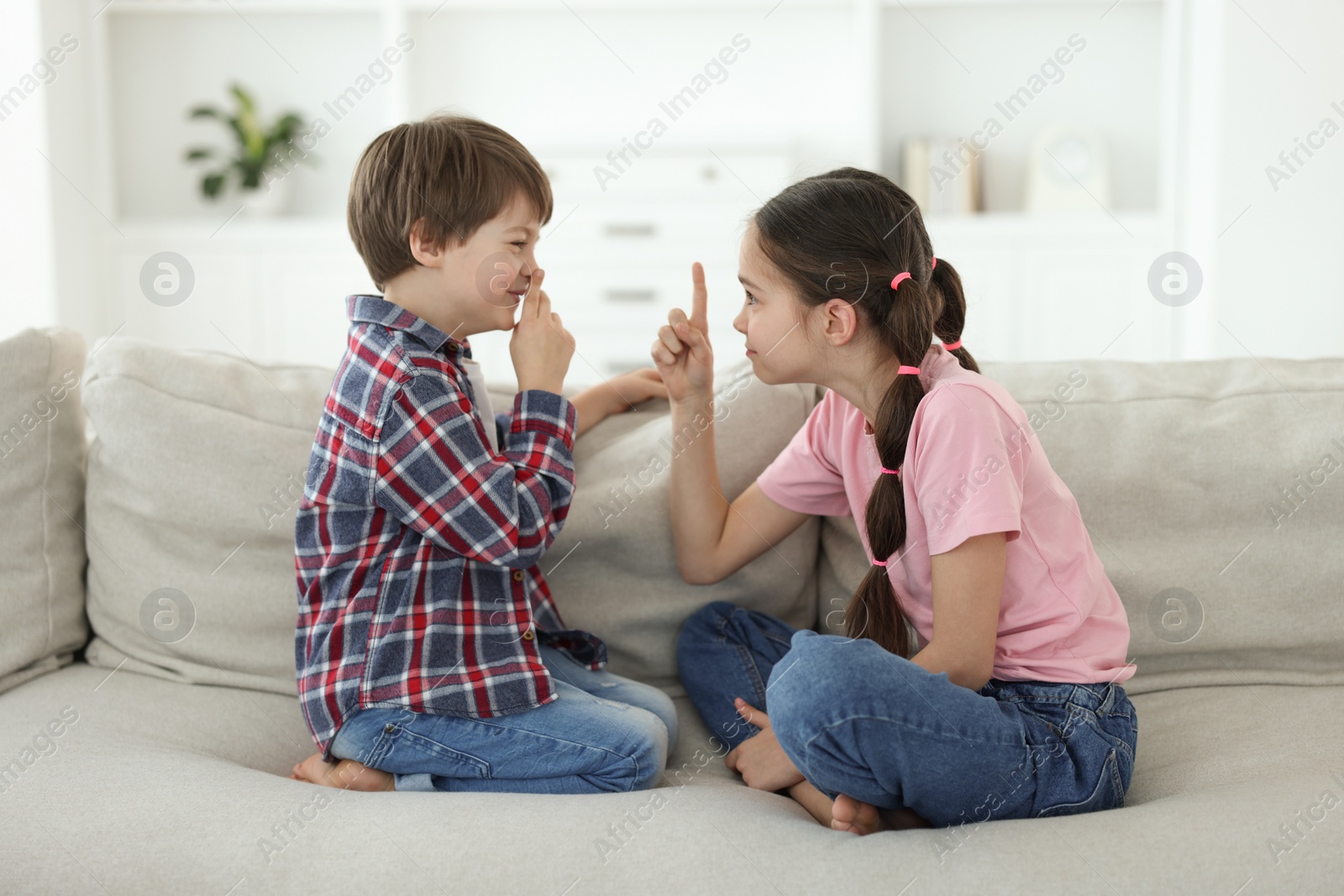 Photo of Upset brother and sister having argument on sofa at home