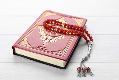 Photo of Muslim prayer beads and Quran on white wooden table, closeup