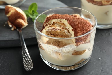 Photo of Delicious tiramisu in glass and spoon on black table, closeup