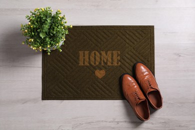 Door mat with word Home, shoes and houseplant on floor, flat lay