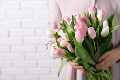 Photo of Woman holding bouquet of tulips against white brick wall, closeup. Space for text
