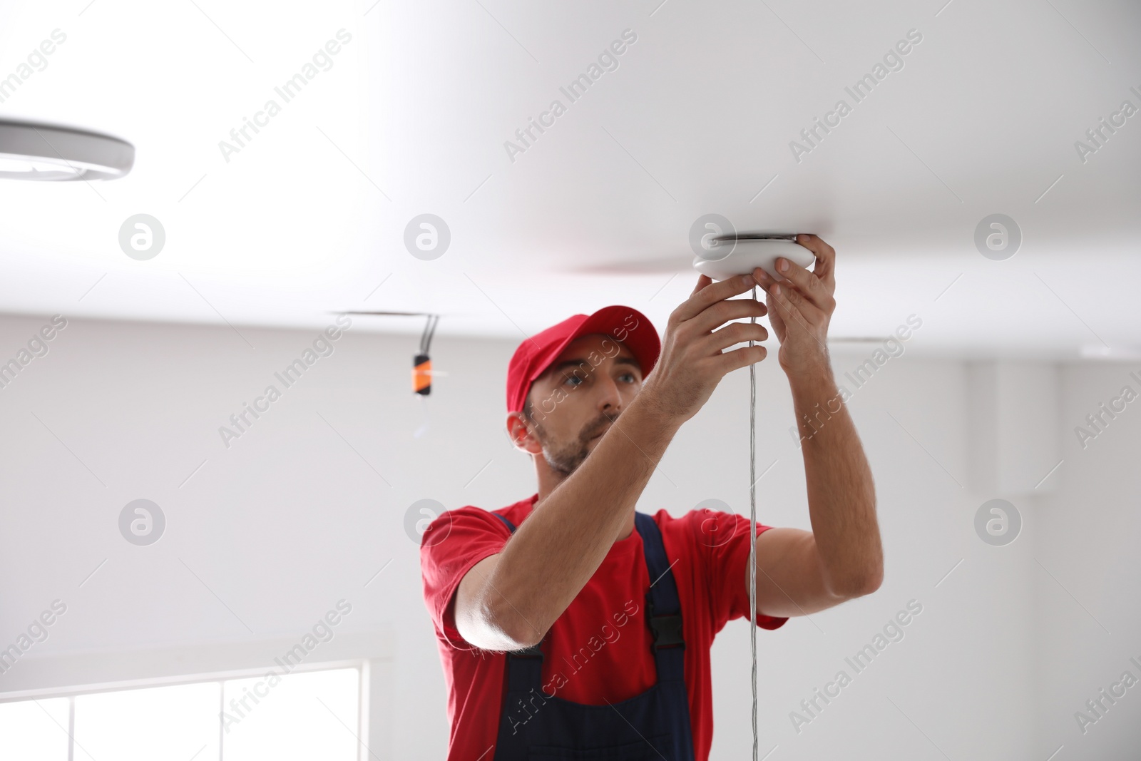 Photo of Worker repairing lamp on stretch ceiling indoors