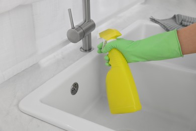 Photo of Woman with spray bottle cleaning water tap in kitchen, closeup