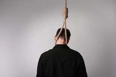 Man with rope noose on neck against light background, back view