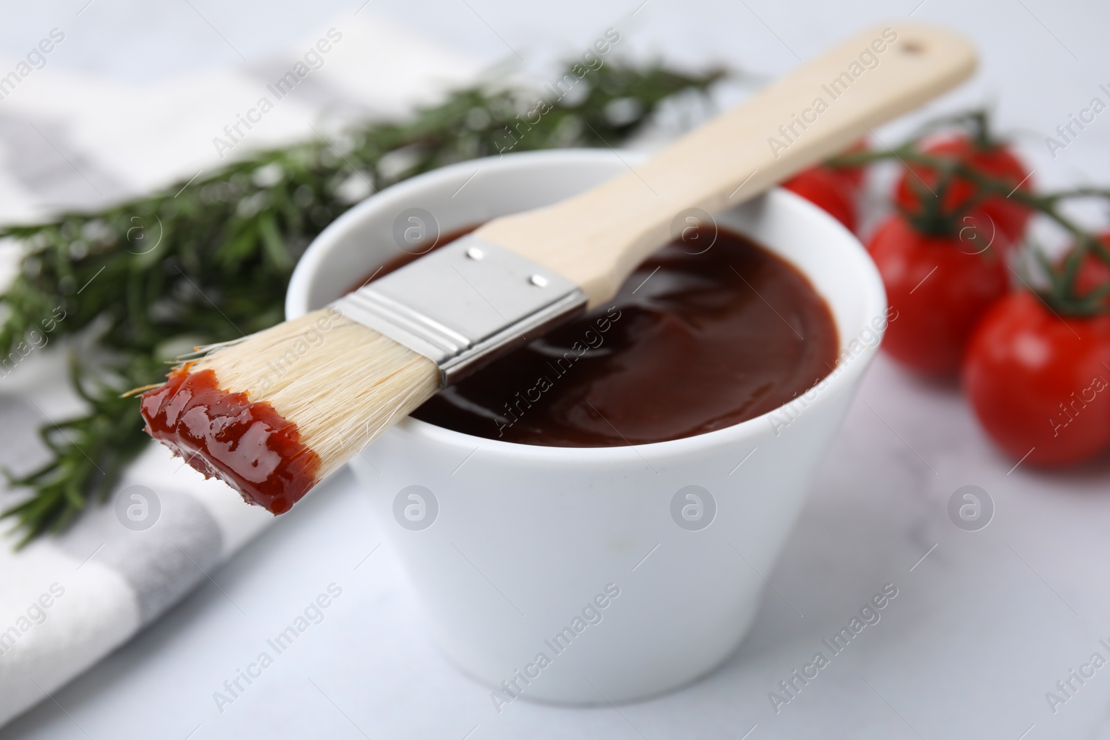 Photo of Marinade in bowl and basting brush on white table, closeup