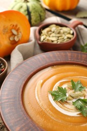 Photo of Delicious pumpkin soup with seeds and parsley in bowl on table, closeup