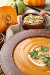 Delicious pumpkin soup with seeds and parsley in bowl on table, closeup