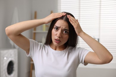 Photo of Emotional woman examining her hair and scalp in bathroom. Dandruff problem