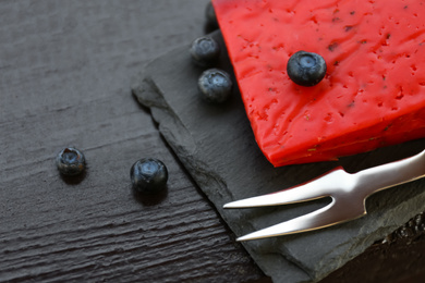 Photo of Delicious red cheese, blueberries and fork on black wooden table, closeup