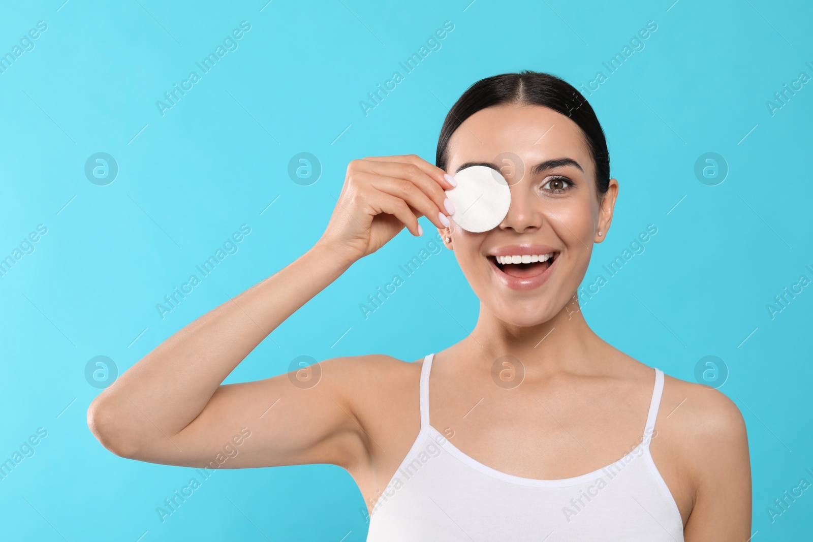 Photo of Young woman using cotton pad with micellar water on light blue background