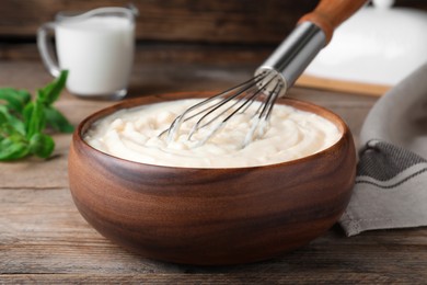 Photo of Whipping pastry cream with balloon whisk on wooden table, closeup
