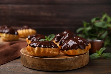 Photo of Delicious profiteroles with chocolate spread and mint on wooden table, closeup
