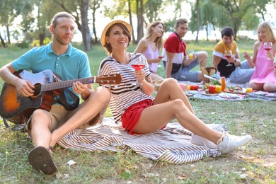 Photo of Young man playing guitar for his girlfriend in park. Summer picnic