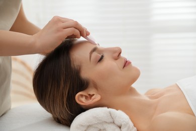 Photo of Young woman receiving facial massage with gua sha tool in beauty salon