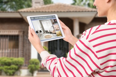 Woman using smart home security system on tablet computer near house outdoors, closeup. Device showing different rooms through cameras