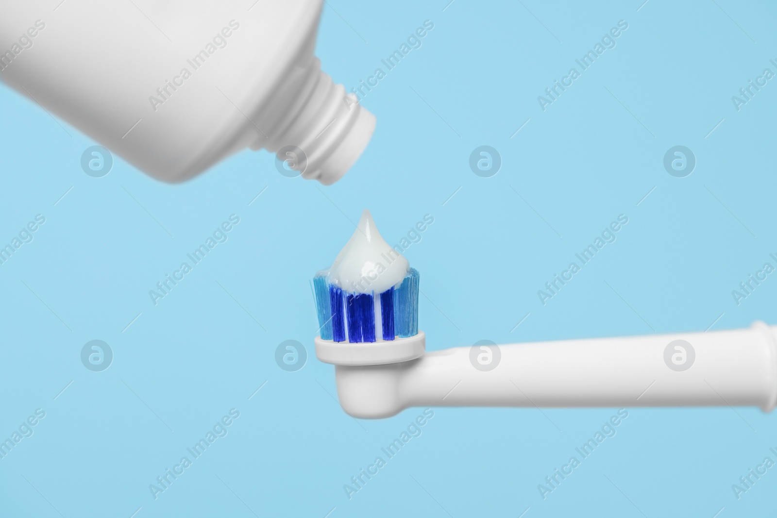 Photo of Electric toothbrush with paste on light blue background, closeup