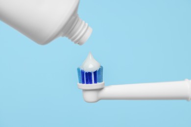 Photo of Electric toothbrush with paste on light blue background, closeup