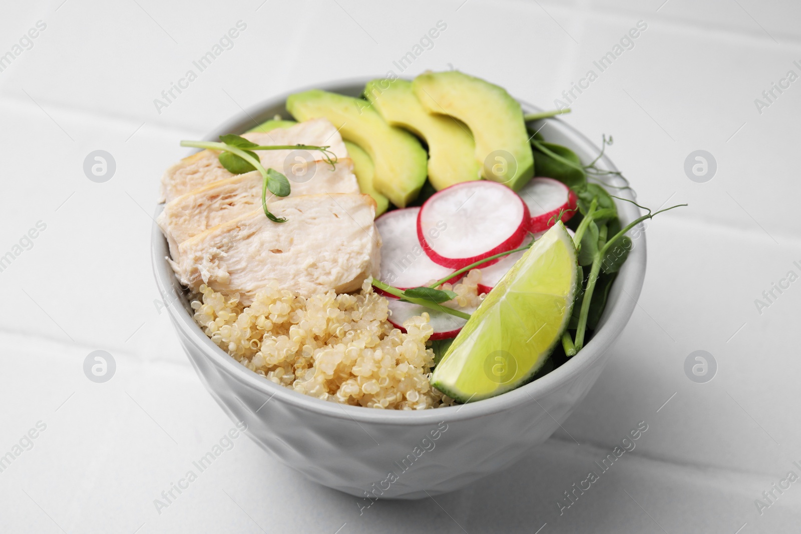 Photo of Delicious quinoa salad with chicken, avocado and radish on white tiled table, closeup