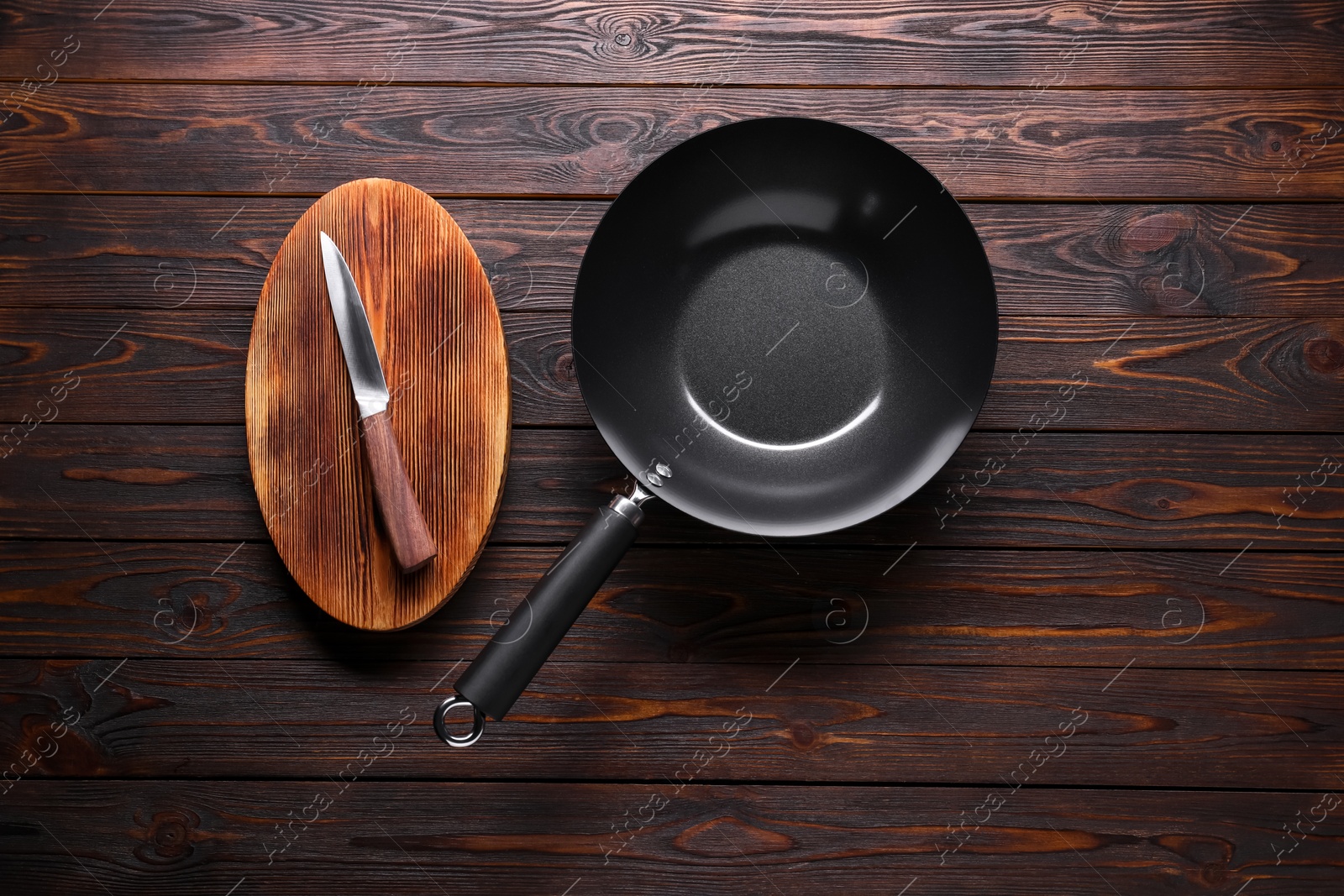Photo of Empty iron wok, knife and cutting board on wooden table, flat lay