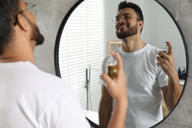 Photo of Man spraying luxury perfume near mirror indoors