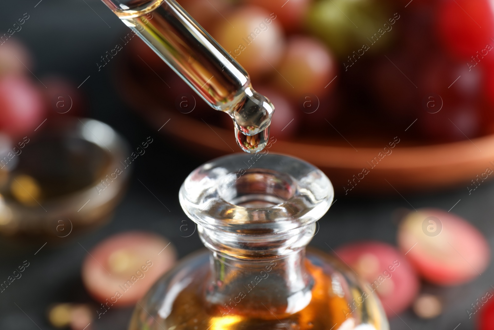 Photo of Dripping natural grape seed oil from pipette into glass bottle on table, closeup. Organic cosmetic