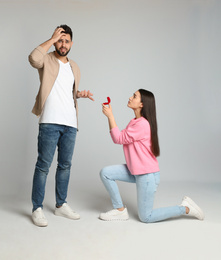 Young woman with engagement ring making marriage proposal to her boyfriend on light grey background