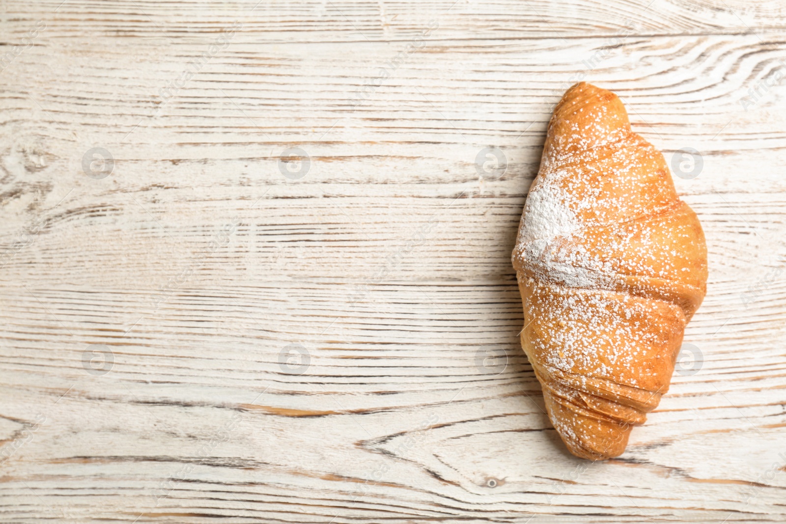 Photo of Tasty croissant with sugar powder on wooden background, top view