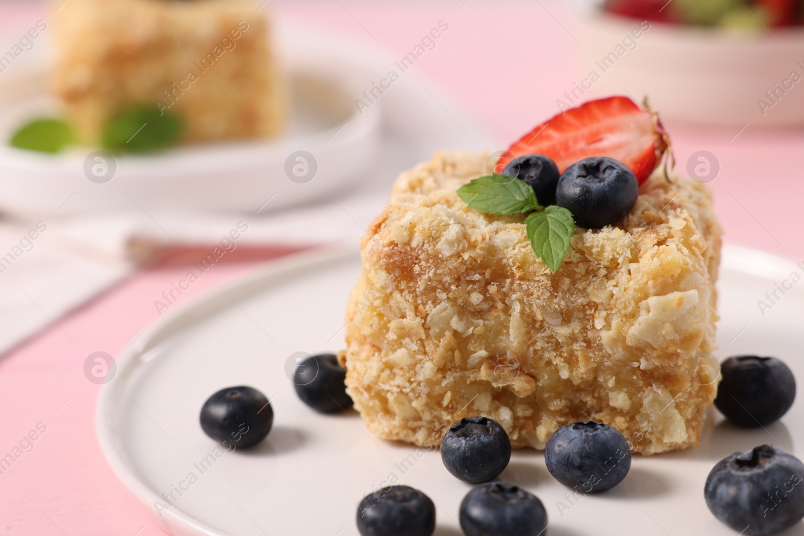 Photo of Piece of delicious Napoleon cake with fresh berries on pink table, closeup. Space for text