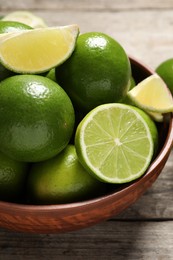 Photo of Tasty ripe limes in bowl on wooden table, closeup