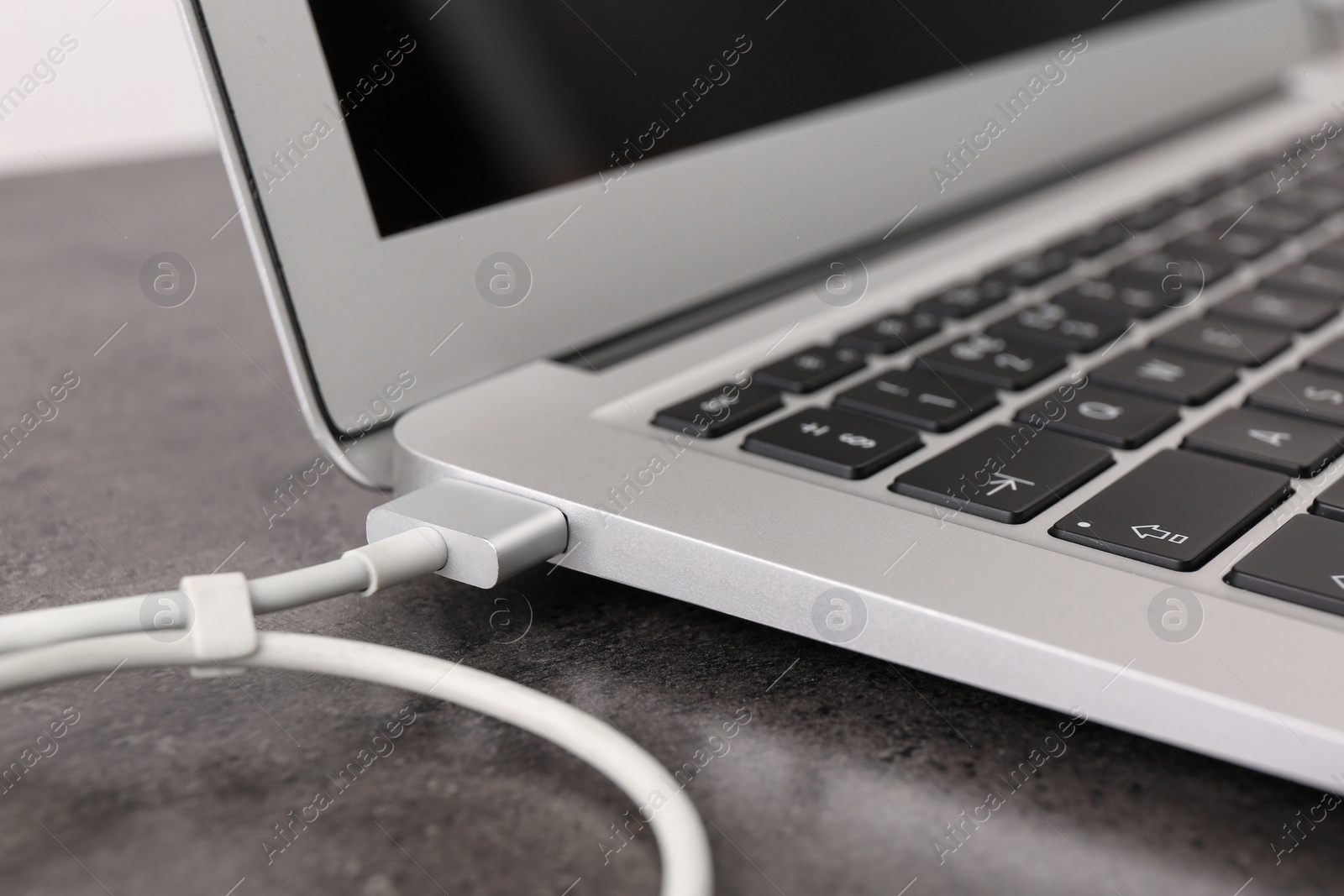 Photo of Modern laptop and charging cable on grey table, closeup