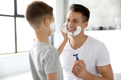 Photo of Son applying shaving foam onto father's face in bathroom