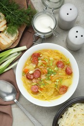 Delicious sauerkraut soup with smoked sausages and green onion served on light grey table, flat lay