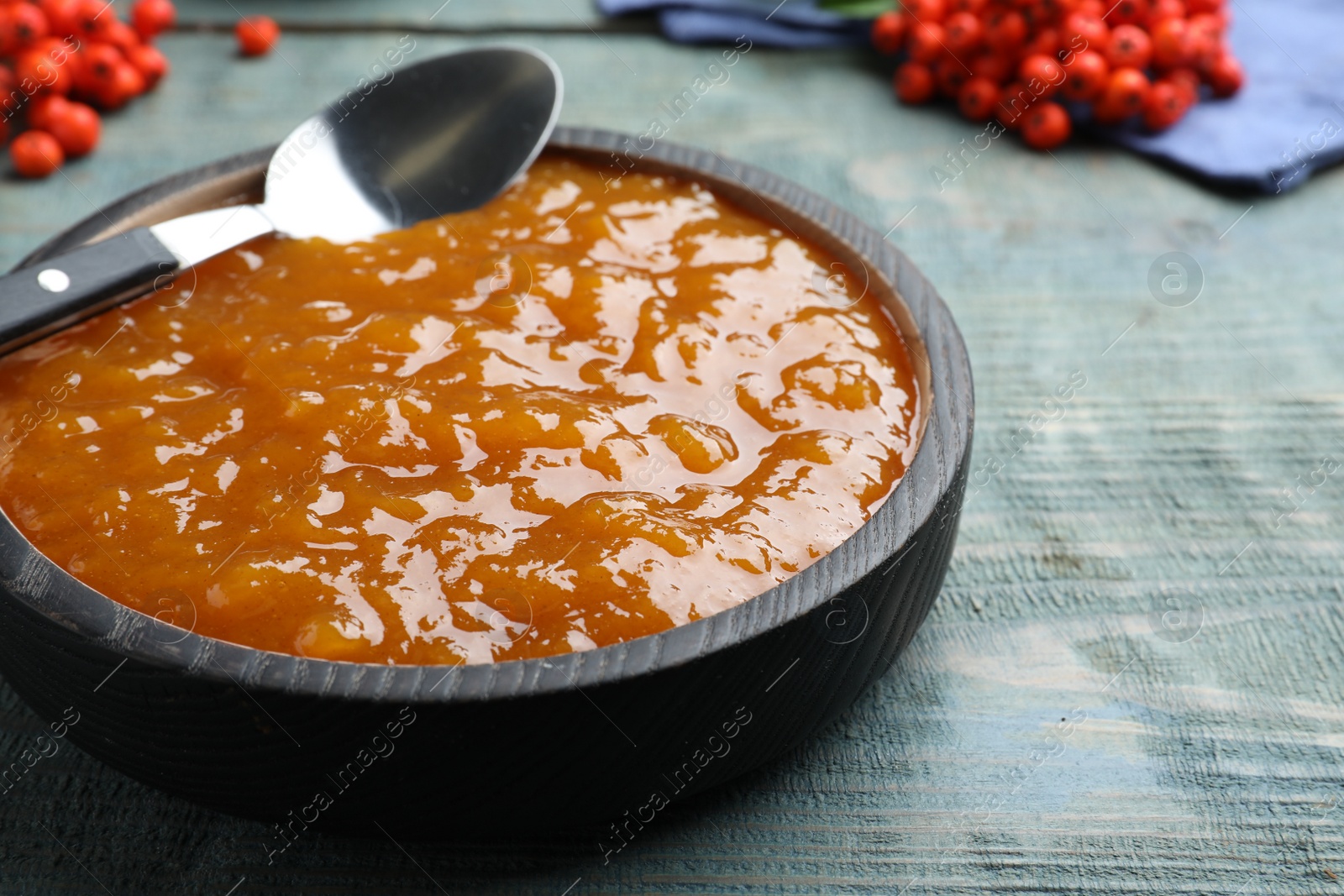 Photo of Delicious rowan jam in bowl on light blue wooden table, closeup