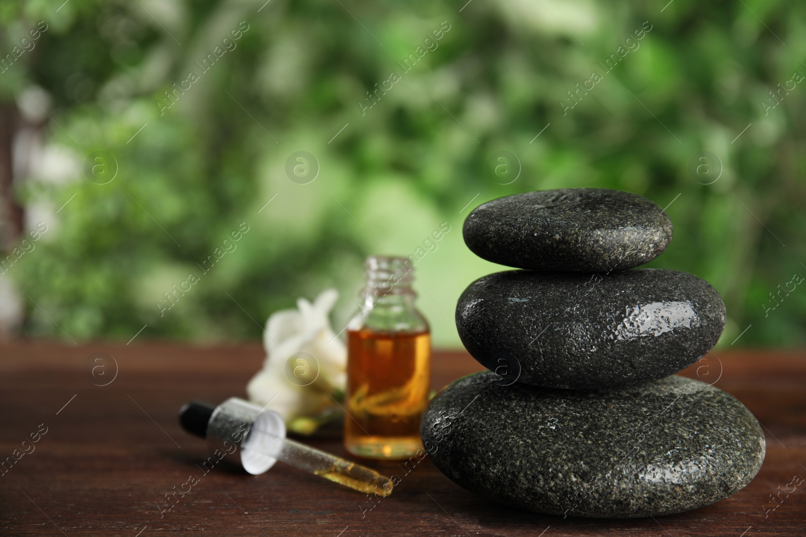 Photo of Stack of grey spa stones, oil and flower on wooden table outdoors, space copy text