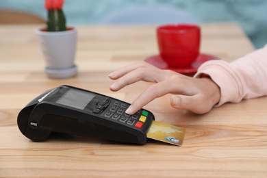 Photo of Woman using card machine for non cash payment at table, closeup