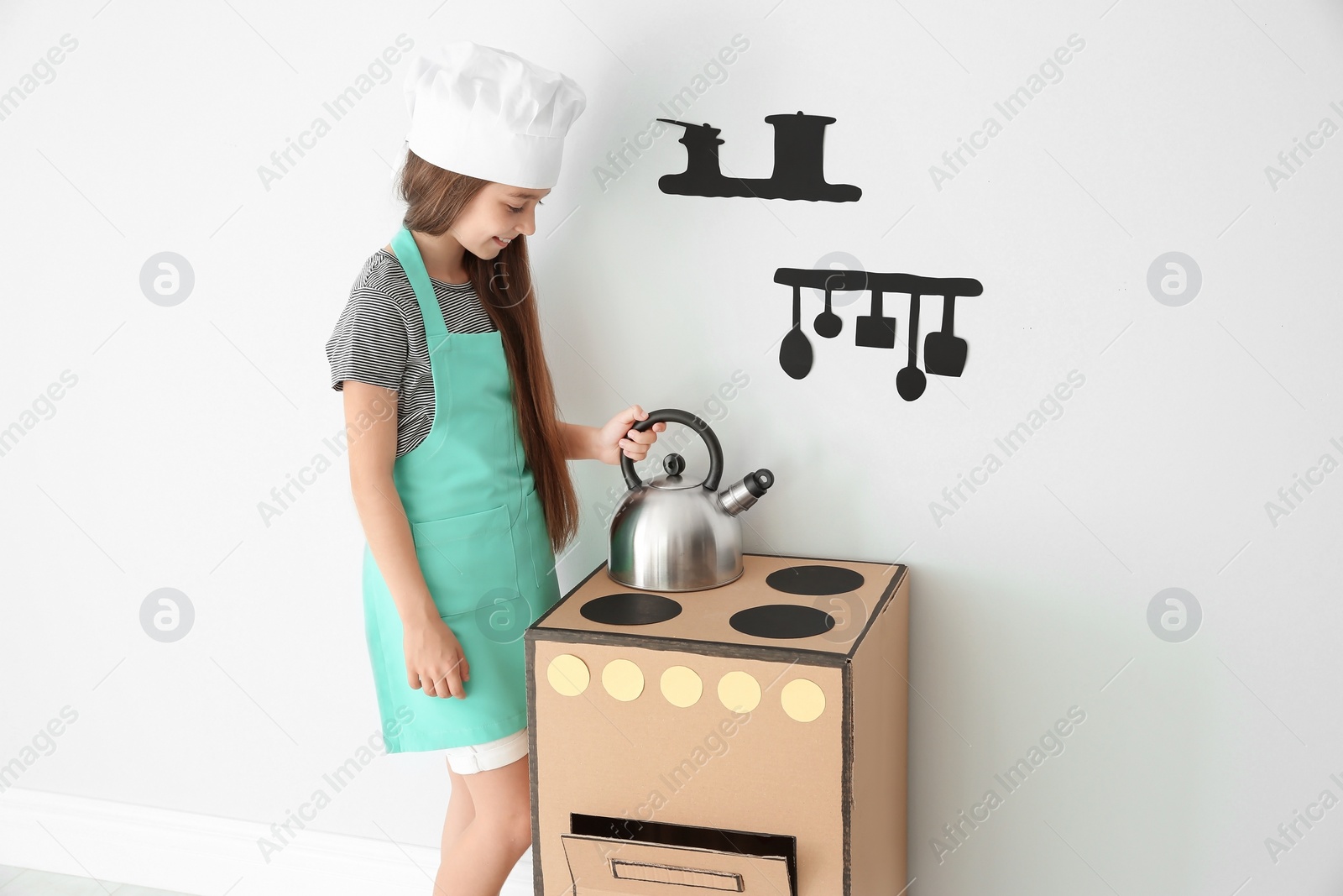 Photo of Little child in chef hat playing with carton stove indoors